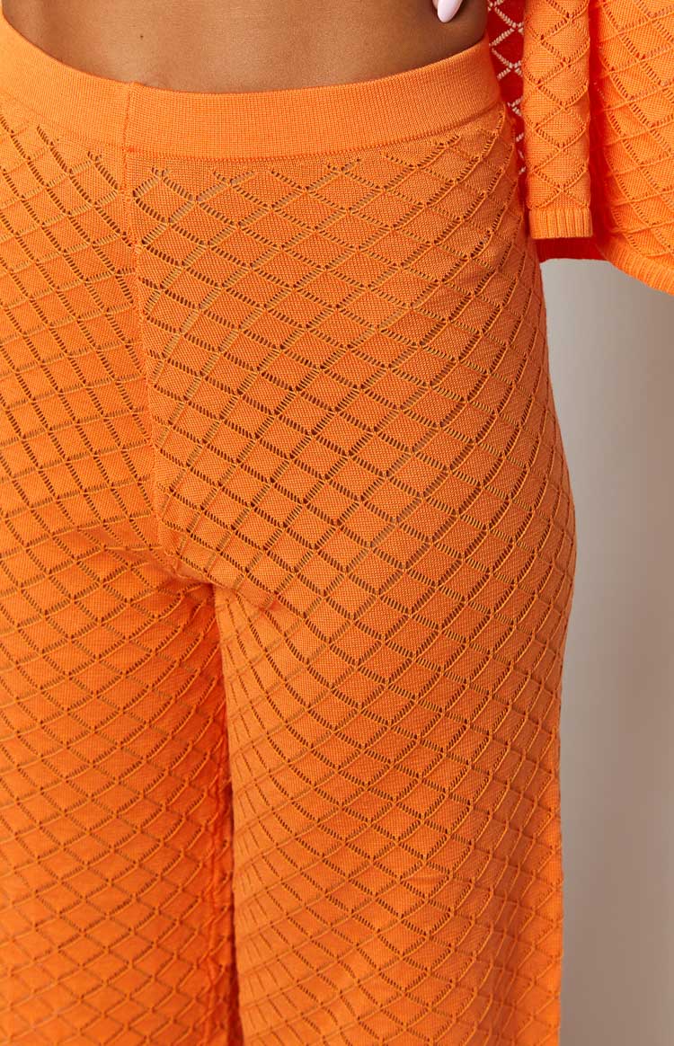Detail shot of the orange knit pants highlighting the open-knit diamond pattern and ribbed waist