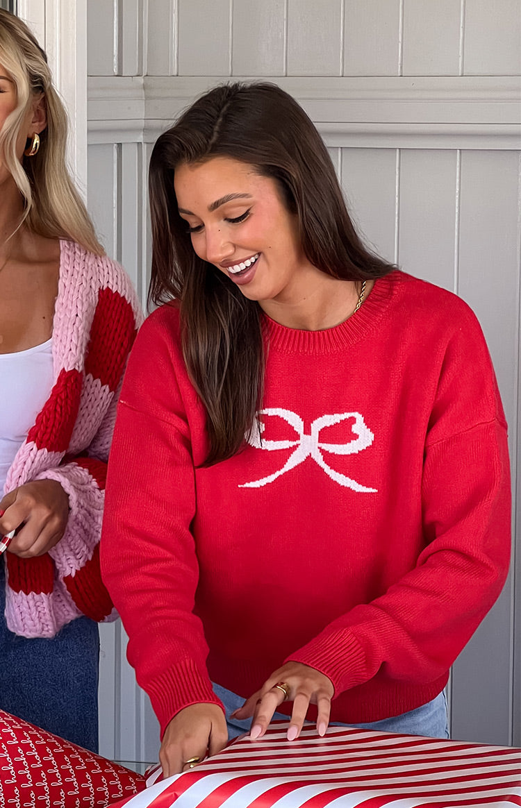 Close-up of a red crew neck sweater with a large white bow graphic on the front and ribbed cuffs