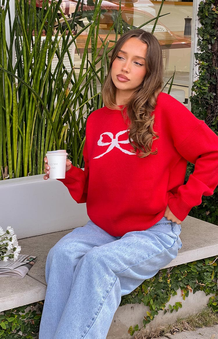 Red knit sweater with a white bow graphic, showing the relaxed fit, ribbed hem, and cuffs