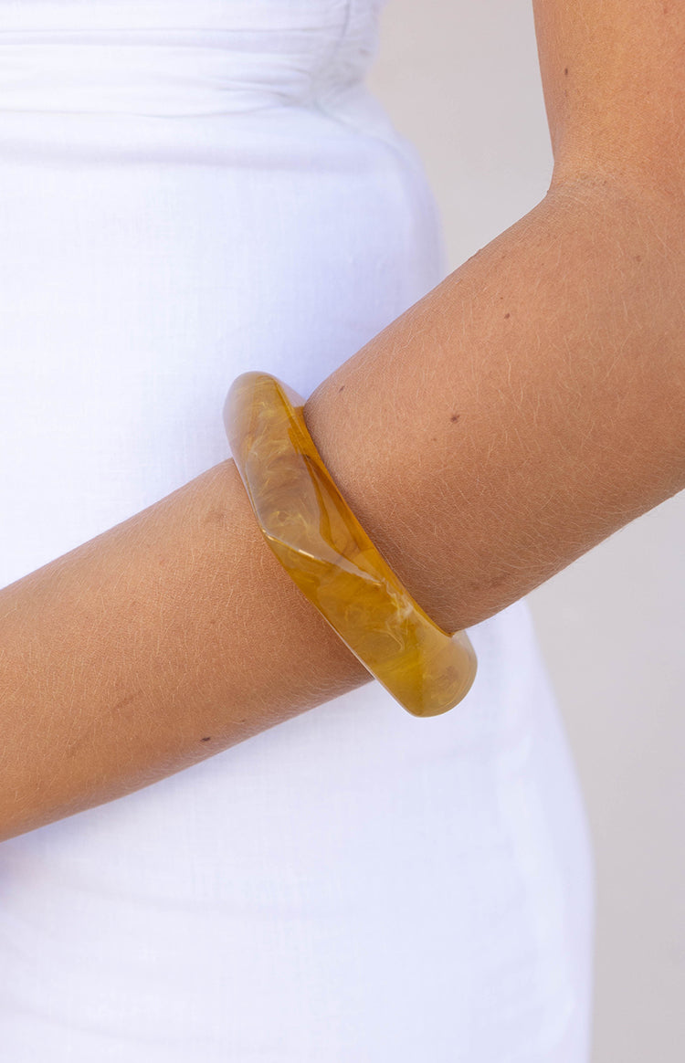 Close-up of the marbled yellow resin square bangle, showing its thick profile and unique pattern