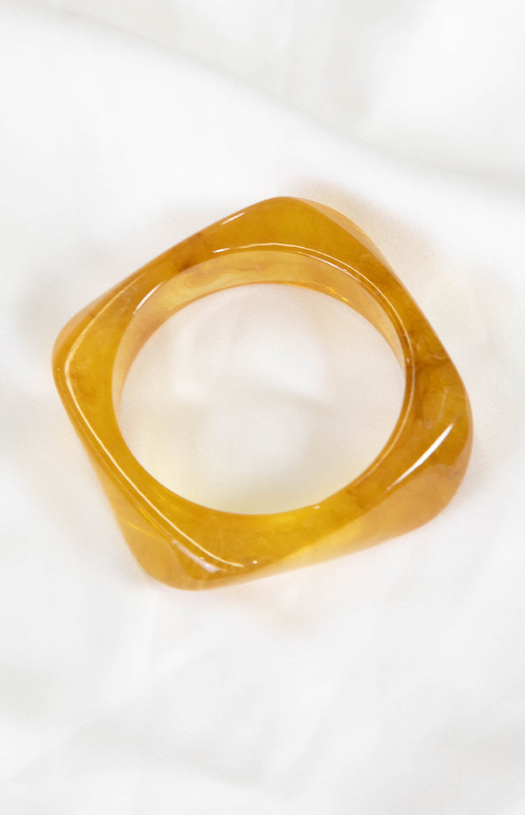 Angled view of a translucent yellow resin square bangle with marbled amber tones and rounded corners
