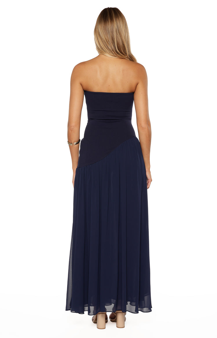 Rear view of a navy strapless maxi dress with a fitted bodice and a flowy skirt with an asymmetrical diagonal seam