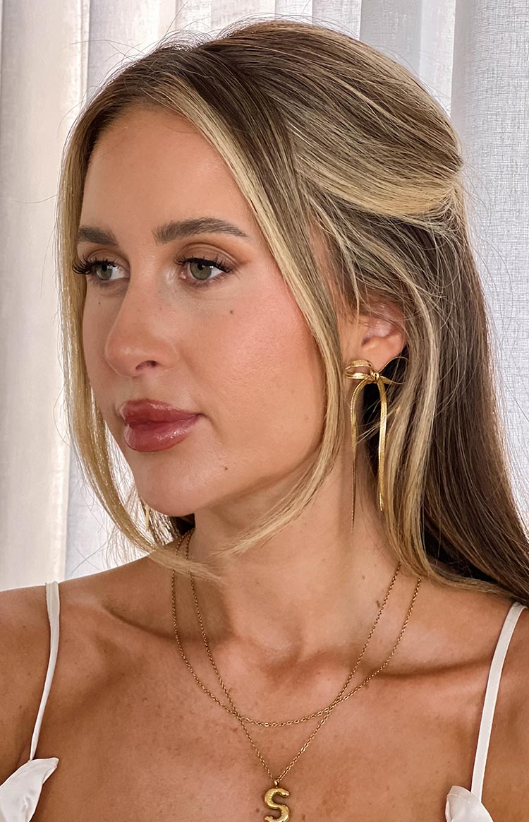 Side view of a gold bow earring with a small bow detail at the top and long, thin, flowing gold strands