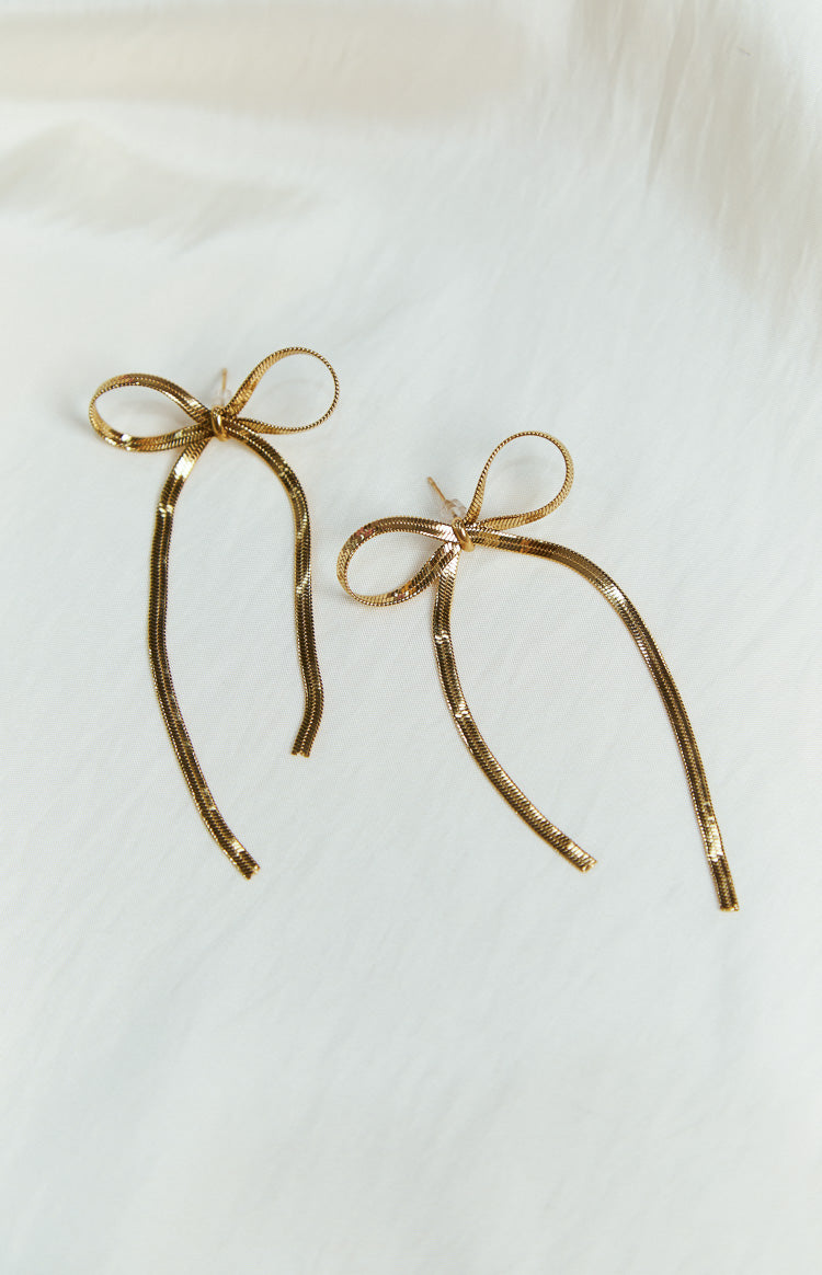 Flat lay of two gold bow earrings, made from snake chain, with long dangling strands