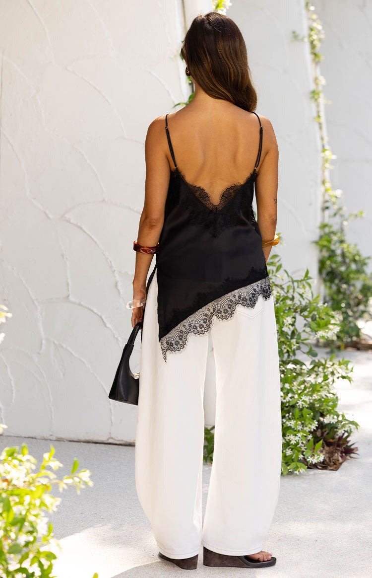 Rear view of a black satin asymmetrical top with a low V-neck back and lace trim along the neckline and hem