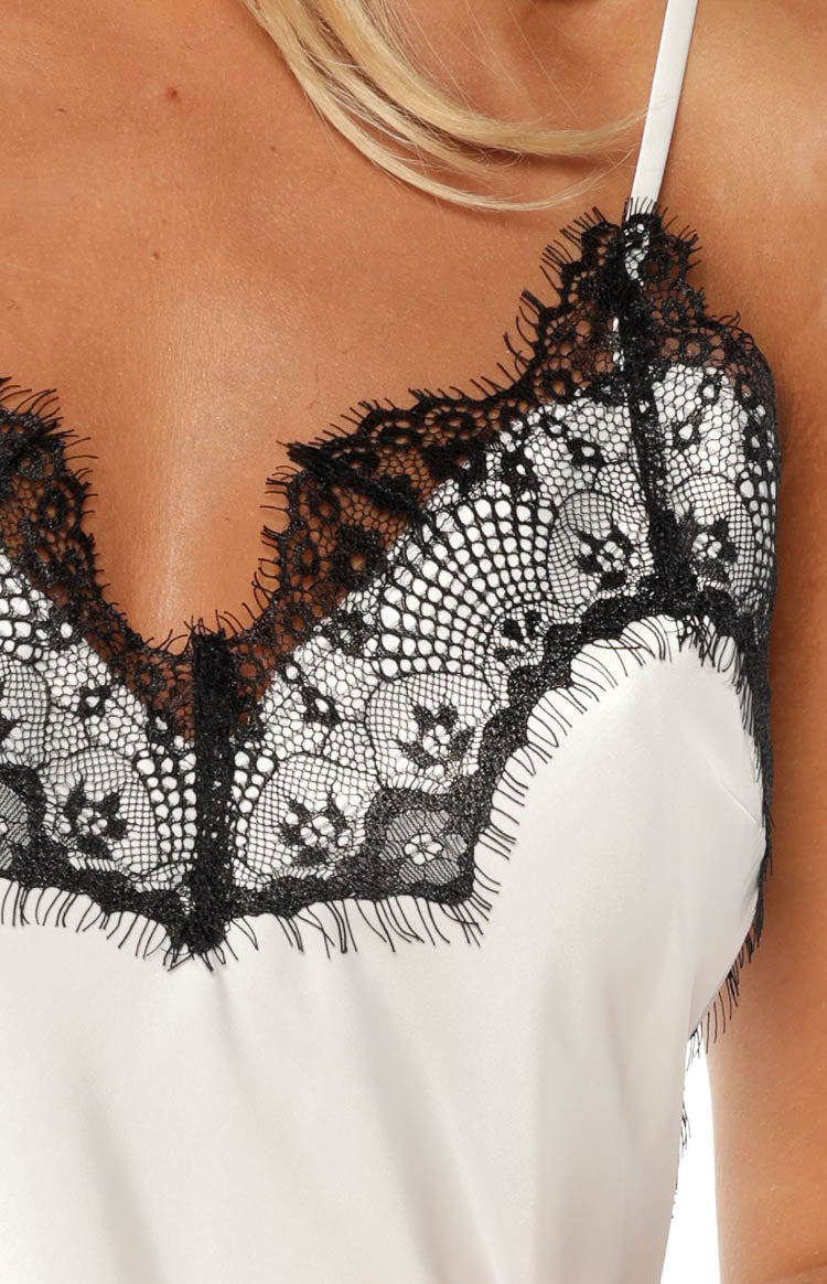 Close-up of the black scalloped lace V-neckline trim on the white satin asymmetrical top
