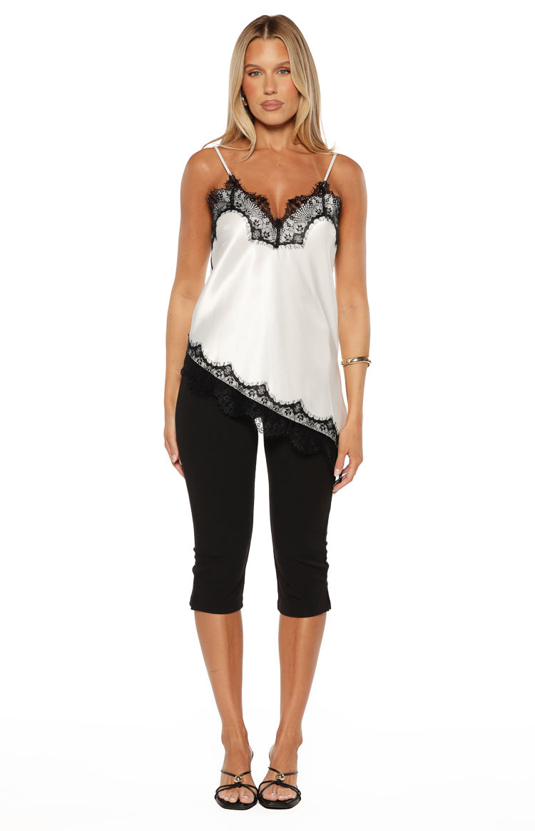 Front view of the white satin asymmetrical top with black lace trim on the V-neck and flowing hem