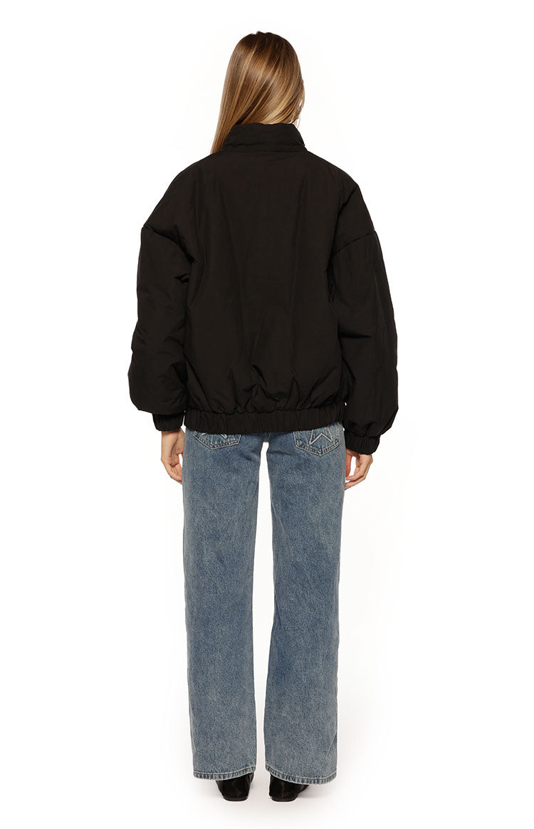 Rear view of a black oversized puffer jacket with a high collar, voluminous sleeves, and elasticated hem and cuffs