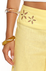 A close-up of light yellow trousers highlighting the wide waistband with cutout flower details and a subtle embroidered border.
