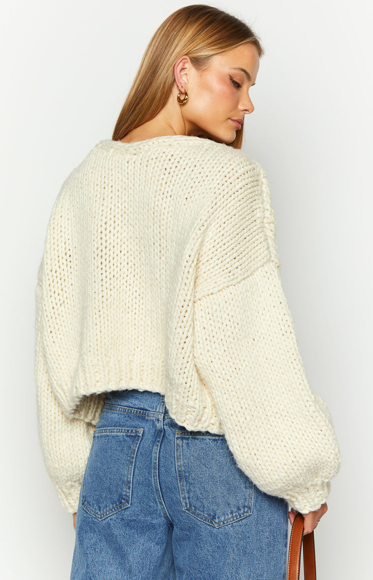 Rear view of a cream chunky knit cardigan with voluminous sleeves and a cropped hem