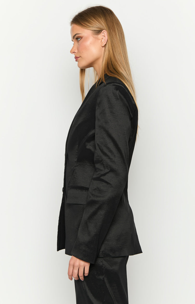 Side view of a black tailored blazer with a subtle textured fabric, showing the lapel, structured shoulder, and flap pocket