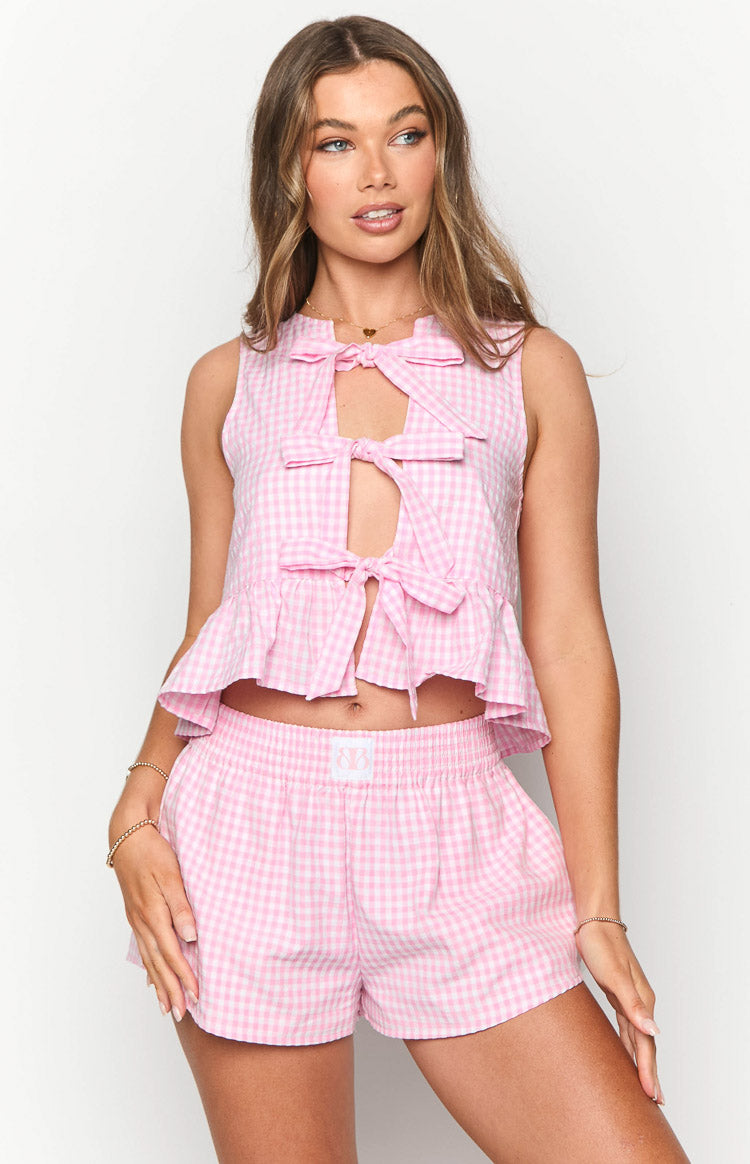 Front view of a pink gingham sleeveless top with a keyhole cutout, three front bows, and a ruffled peplum hem