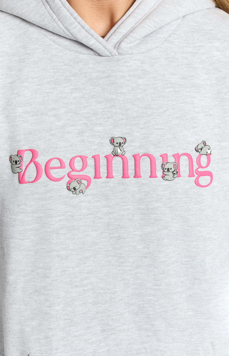 Close-up of the grey marl hoodie showing pink embroidered "Beginning" text with small koala illustrations