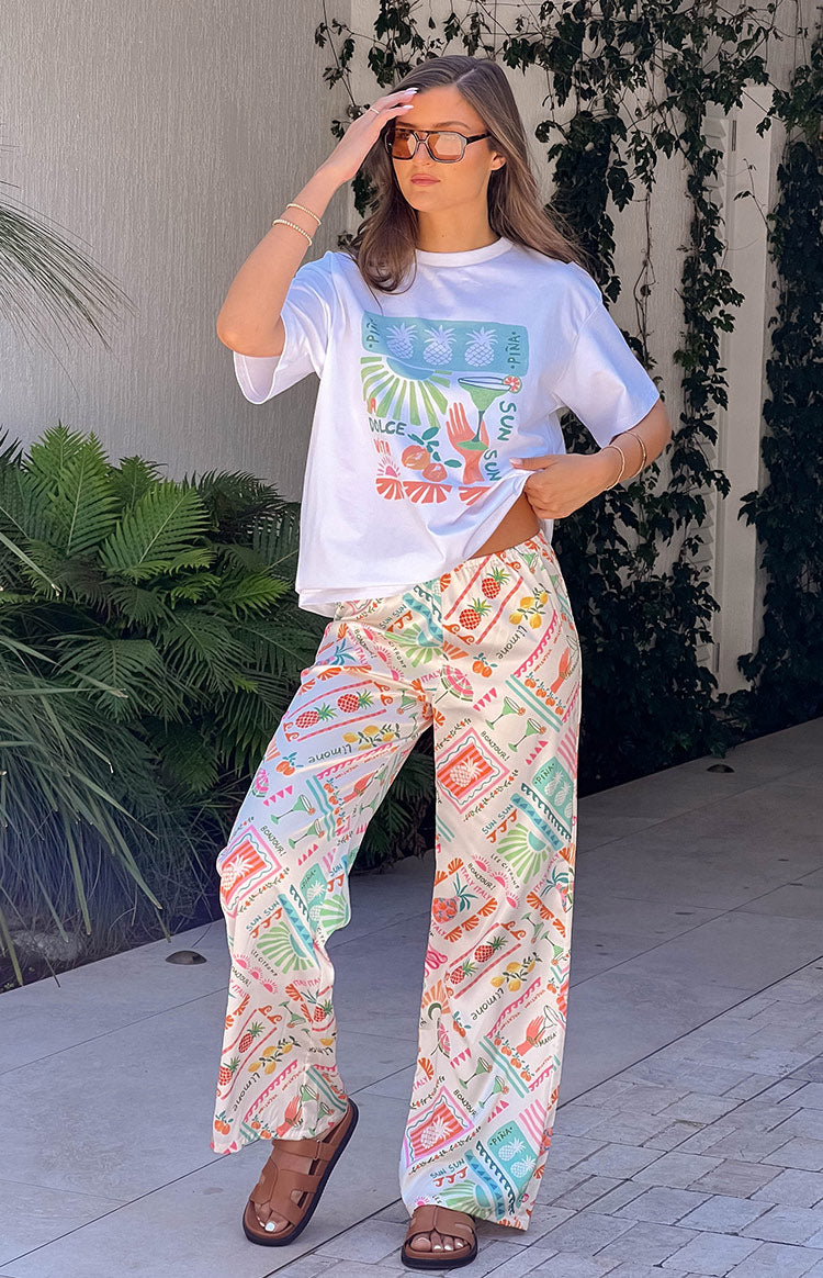 Full-length view of white wide-leg pants with a colourful Dolce Vita print featuring pineapples and cocktails