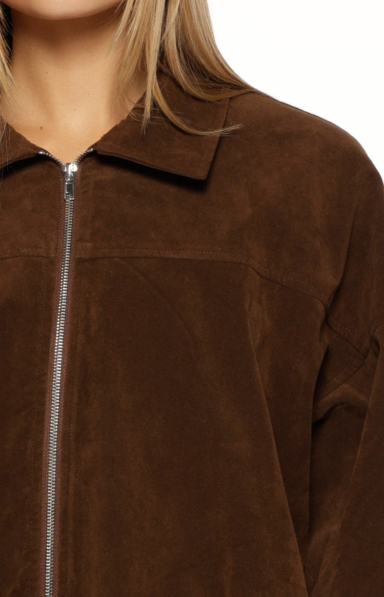 Close-up of the brown suedette bomber jacket showing the silver front zipper, pointed collar, and soft texture