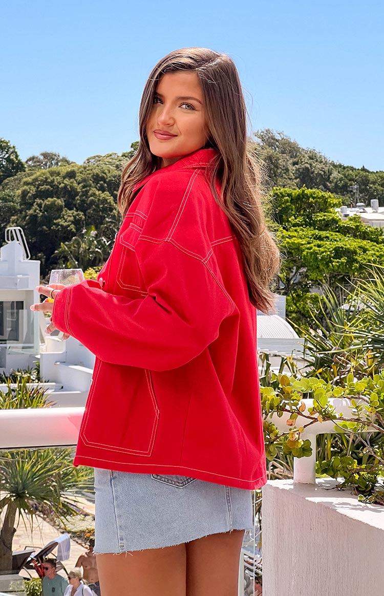 Side view of a red denim jacket with white contrast stitching and a relaxed fit