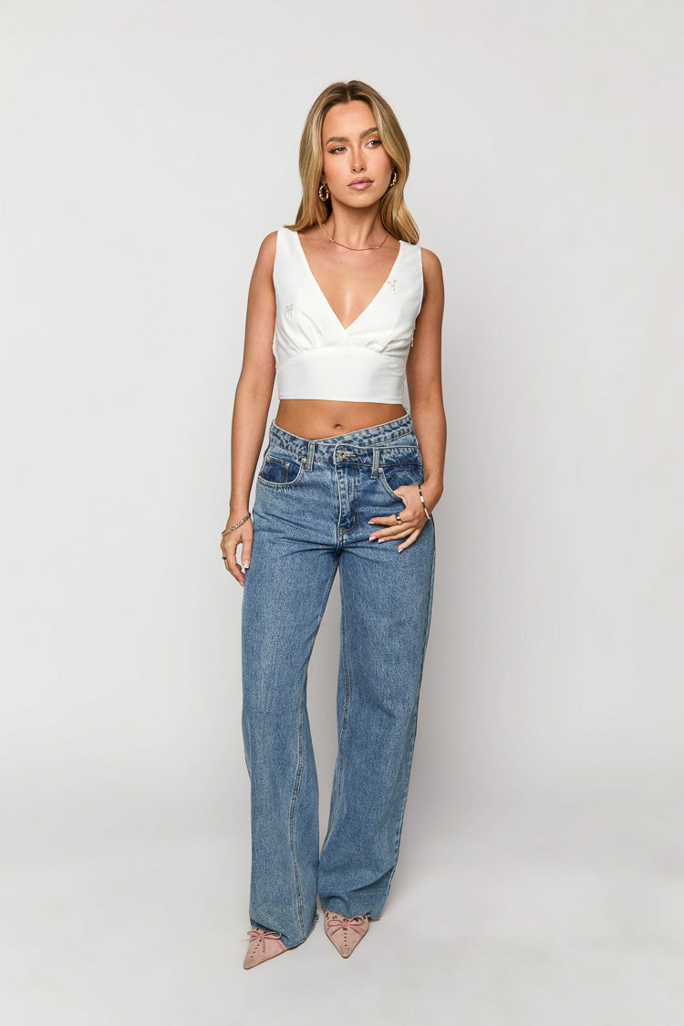 Front view of a white sleeveless wrap V-neck crop top with subtle floral embellishments