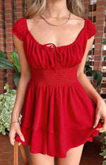 Close-up of the red playsuit showing the off-shoulder neckline, front tie detail, smocked elastic waist, and tiered ruffle shorts