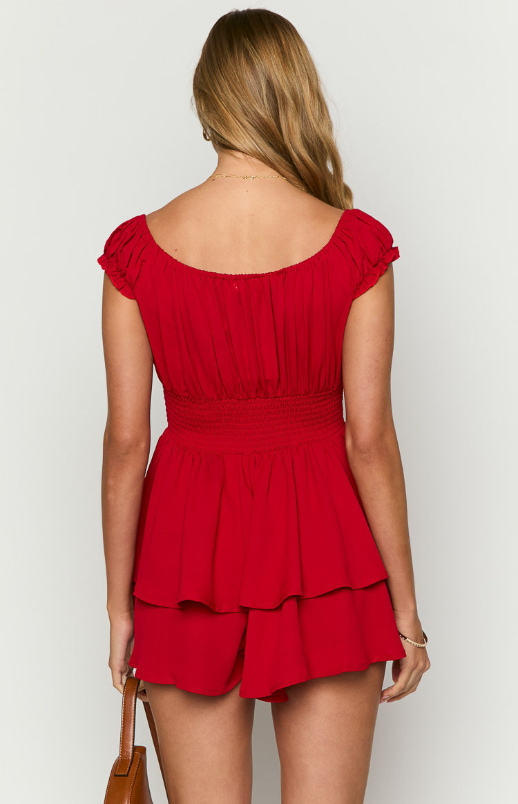 Rear view of a red playsuit with an off-shoulder neckline, gathered short sleeves, shirred waist, and tiered ruffle shorts