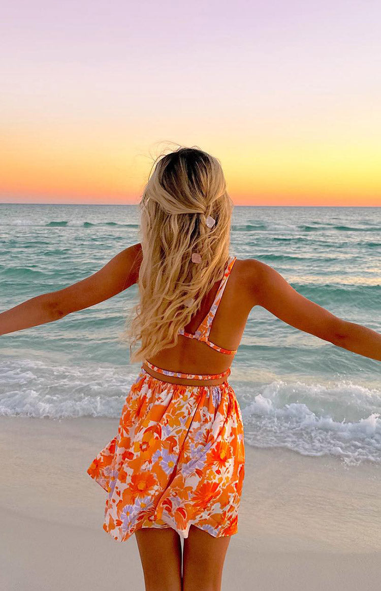 Rear view of an orange floral mini dress with a cut-out back, thin straps, and a flowy mini skirt
