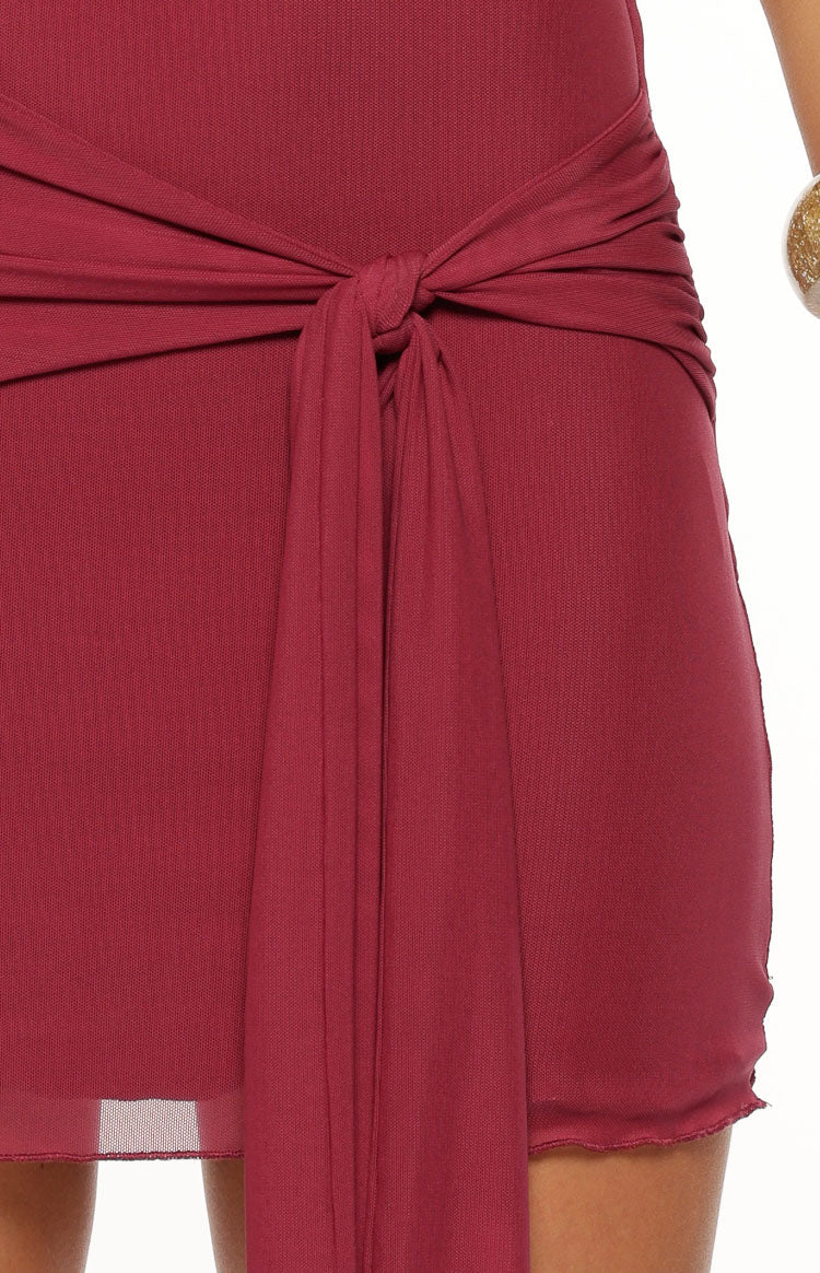 Close-up of the burgundy mini dress showing the wrap tie knot detail at the waist and raw edge hem