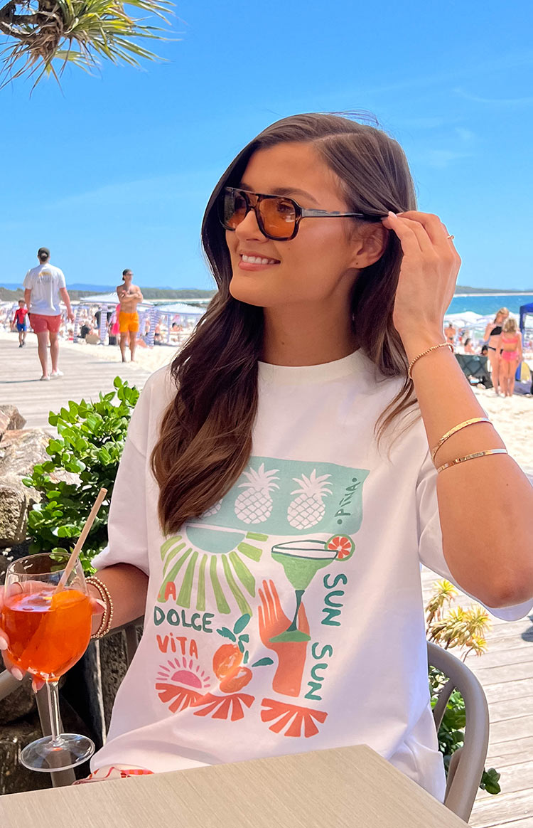Close-up of the white tee's colourful graphic print with 'Dolce Vita' text, pineapples, margarita glass, and sun