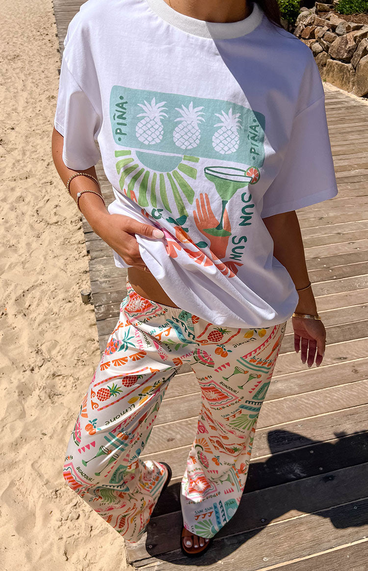 Front view of a white oversized tee with a colourful graphic print featuring pineapples, sun, and cocktail