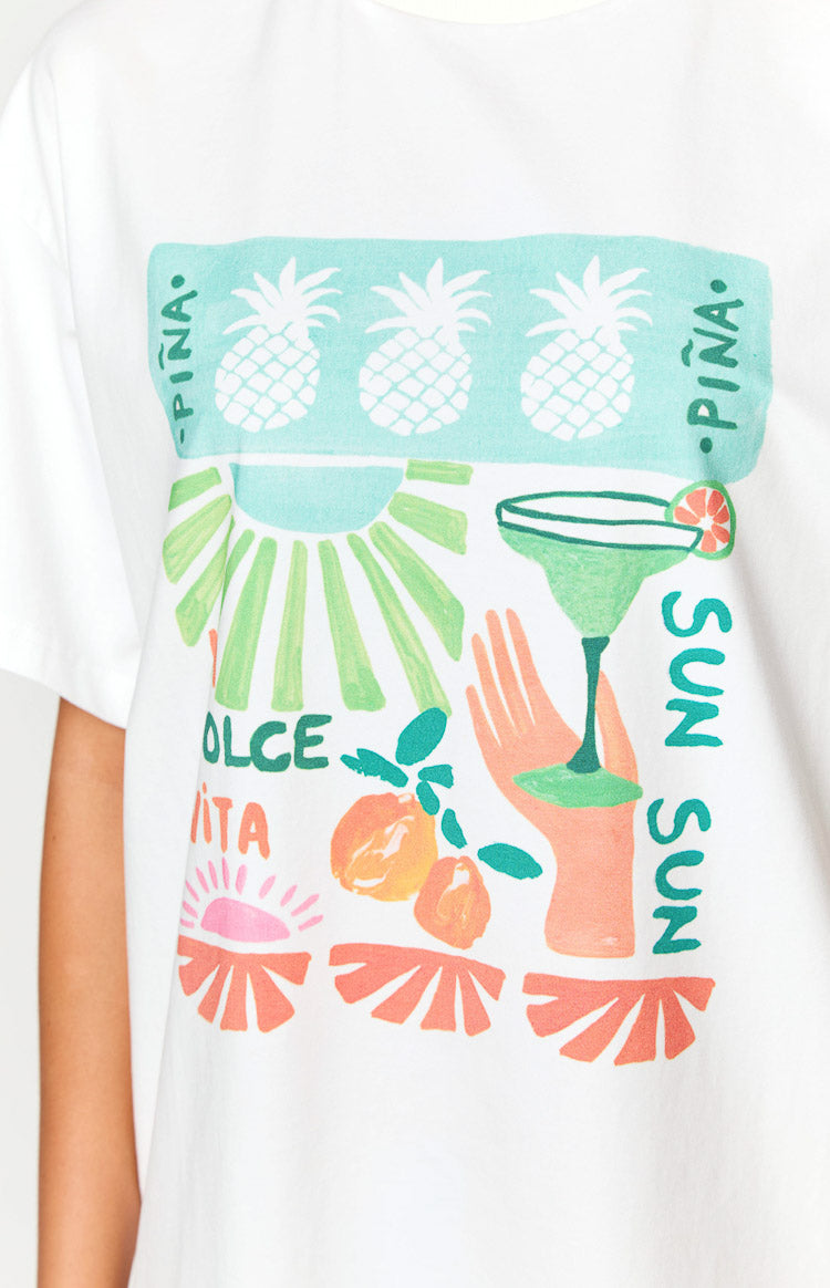 Close-up of the white tee's colorful print: pineapples, sun rays, margarita, citrus, and 'PINA', 'DOLCE VITA', 'SUN' text