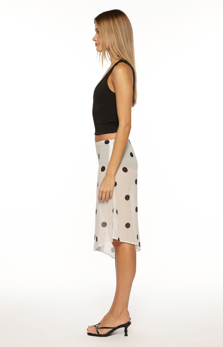Side view of a white sheer midi skirt with black polka dots and an asymmetrical hem