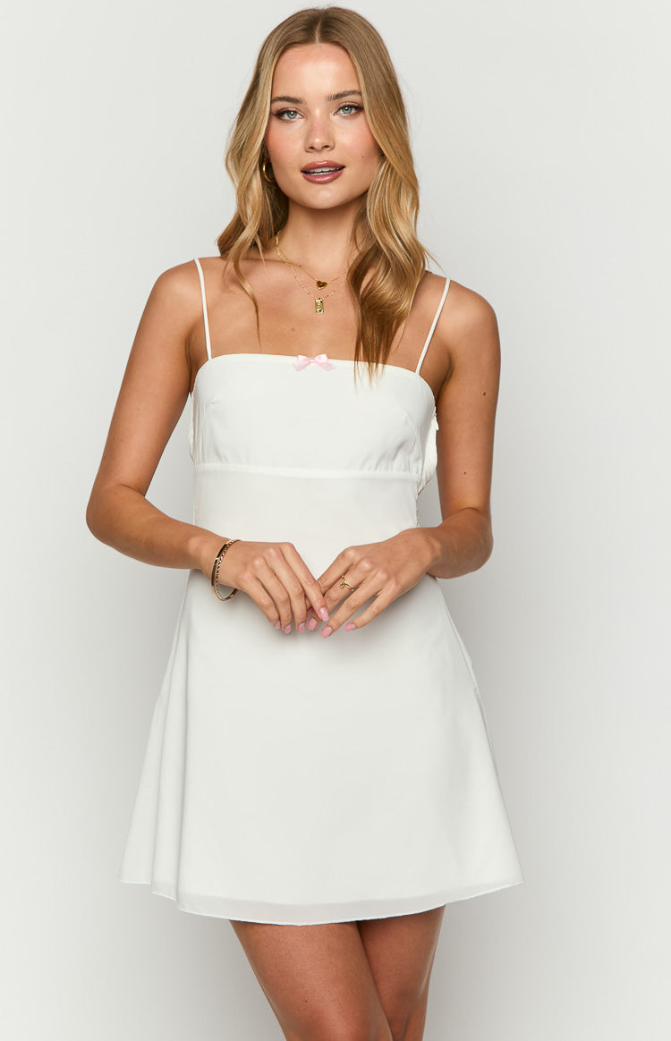 White mini dress with a square neckline, thin spaghetti straps, and a small pink bow detail at the bust