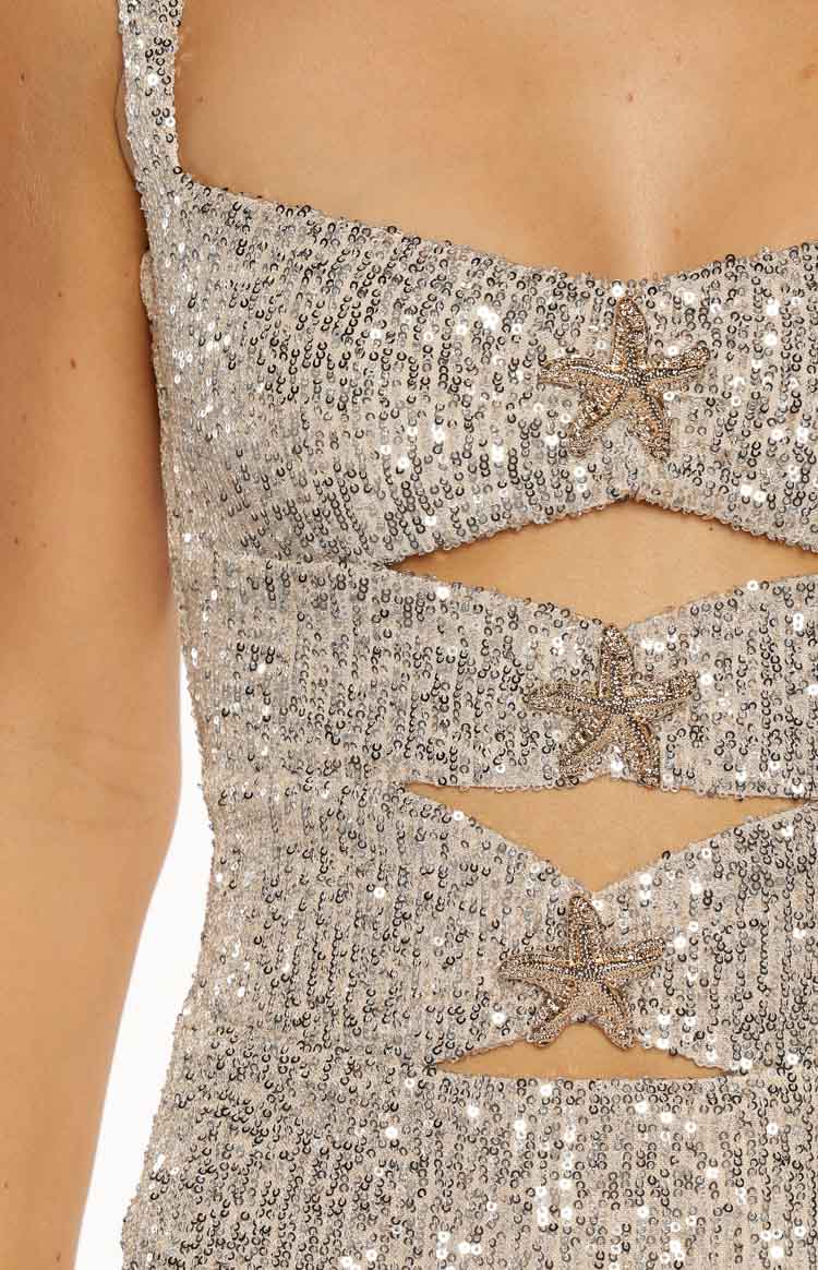 A very close up vertical shot detailing the bodice and waist of a silver colored sequin mini dress. The image focuses on the two horizontal cutouts which are separated by a band of fabric. Both bands as well as the fabric above the top cutout are decorated with small beaded starfish appliqués giving a subtle nautical theme.