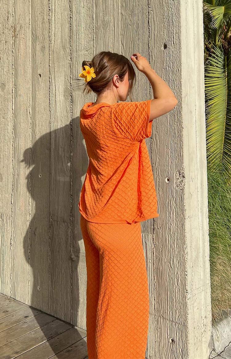 Rear view of an orange textured knit top with a collar and short sleeves, showing the diamond pattern