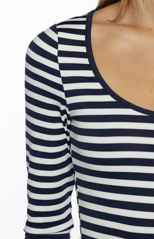 A tightly cropped close-up focuses on the shoulder and chest of our model wearing a fitted long-sleeve top. This knit top features a classic nautical pattern of navy blue and white horizontal stripes. The neckline is a wide scoop neck trimmed with a thin navy blue band.