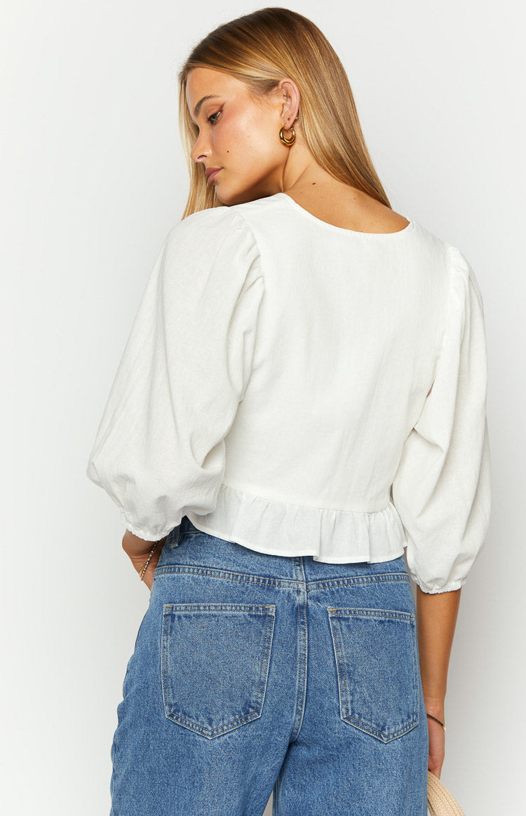 Rear view of a white textured top with 3/4 puff sleeves and a ruffled hemline