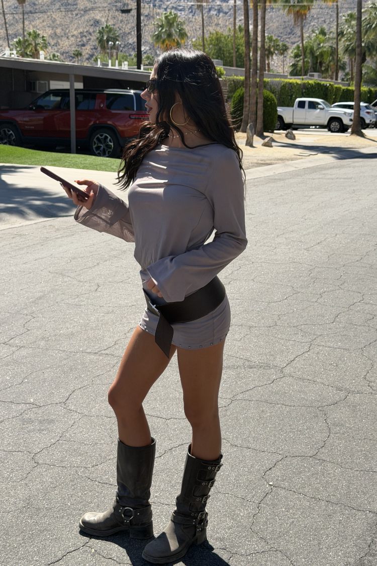 Side view of a brown sheer mesh mini dress with long flared sleeves and stud hem detail