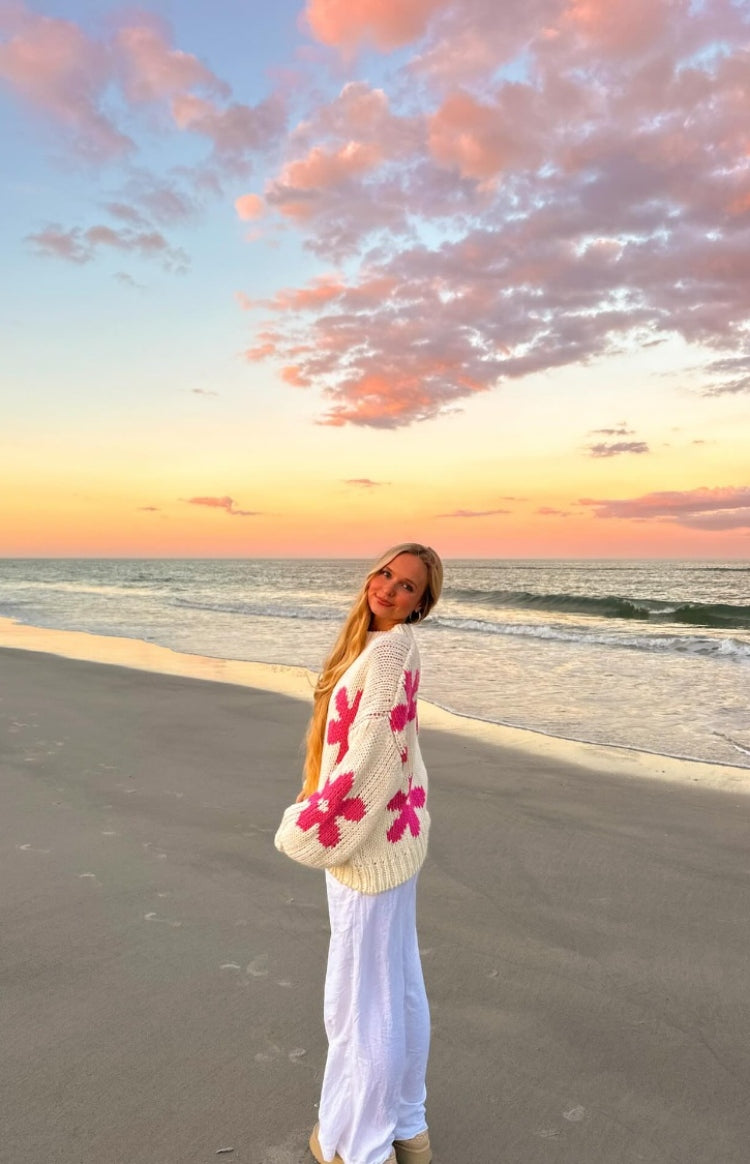 Side view of a cream knit sweater with large pink flower patterns and ribbed cuffs