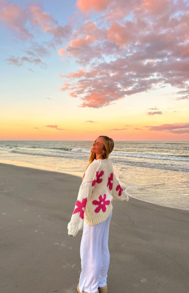Rear side view of an oversized cream chunky knit sweater with large scattered pink flower patterns