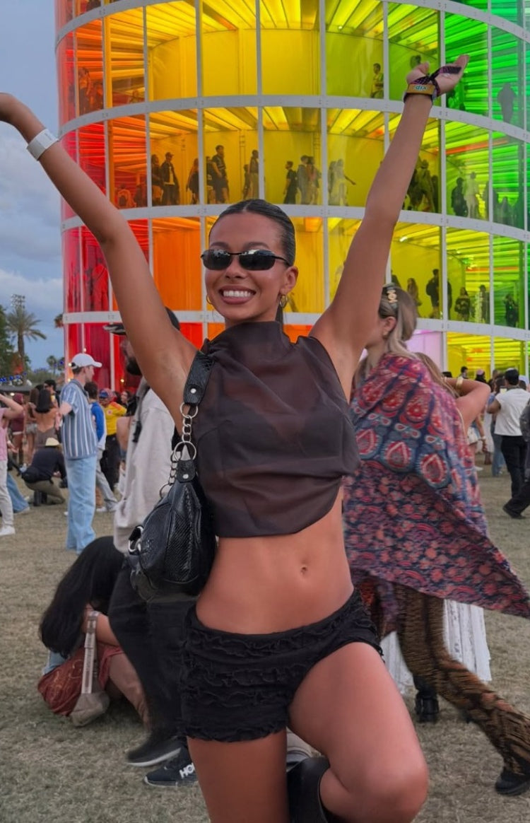 Front view of a black sheer high neck sleeveless crop top with a loose, draped hem