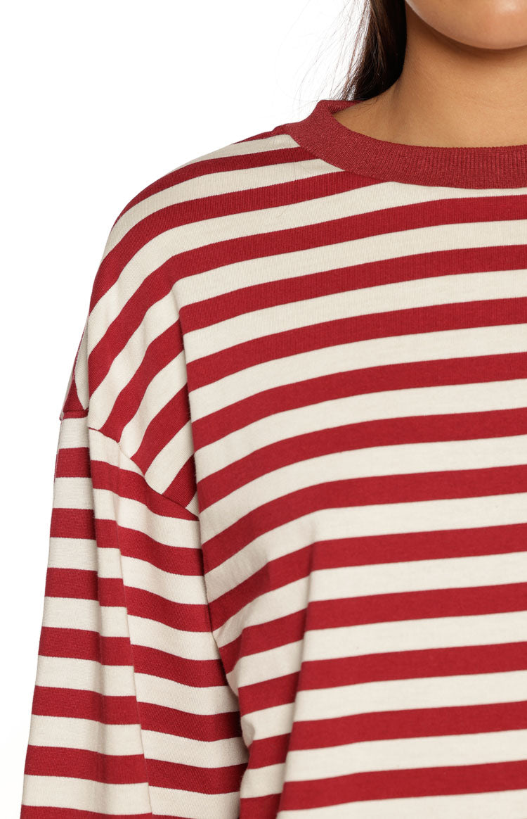 A close-up focusing on the shoulder of a long-sleeved top featuring evenly spaced horizontal stripes in deep red/burgundy and off-white. This top has a relaxed fit with a dropped shoulder seam a ribbed crewneck collar in solid deep red and the texture suggests a soft knit or jersey fabric.