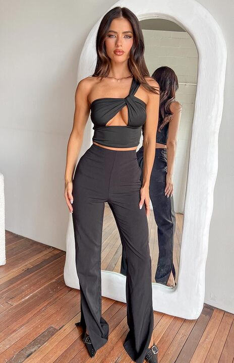A lifestyle shot of our model wearing high-waisted black trousers. This pants feature a slim fit through the hips and a long wide-leg silhouette that pools slightly at the feet.