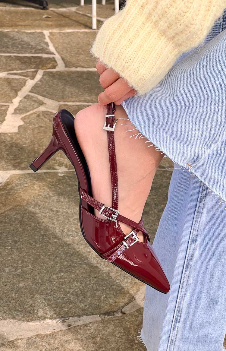 Close-up of the red patent slingback heel showing the multiple buckled straps across the foot and pointed toe