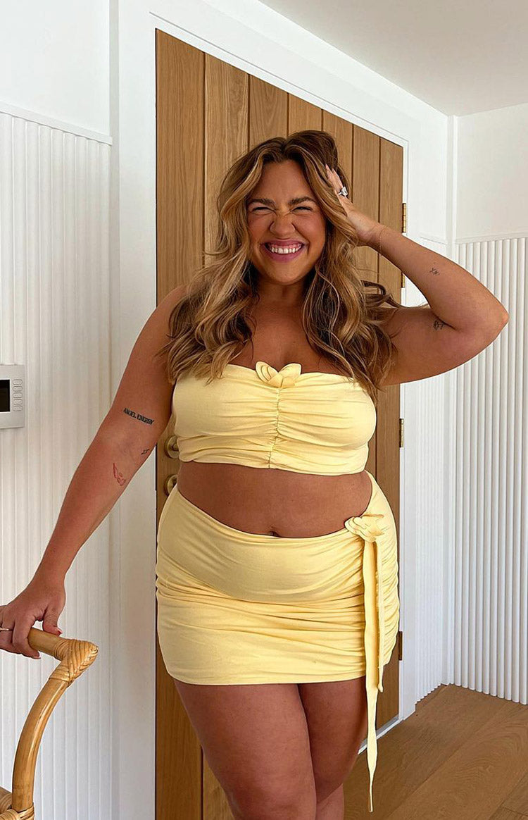 Front view of a yellow strapless cropped top with a ruched bodice and a butterfly detail at the bust