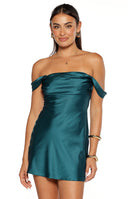 Our model wearing a short dark teal satin mini-dress with an off-the-shoulder neckline featuring ruched draped sleeves and a fitted bodice.