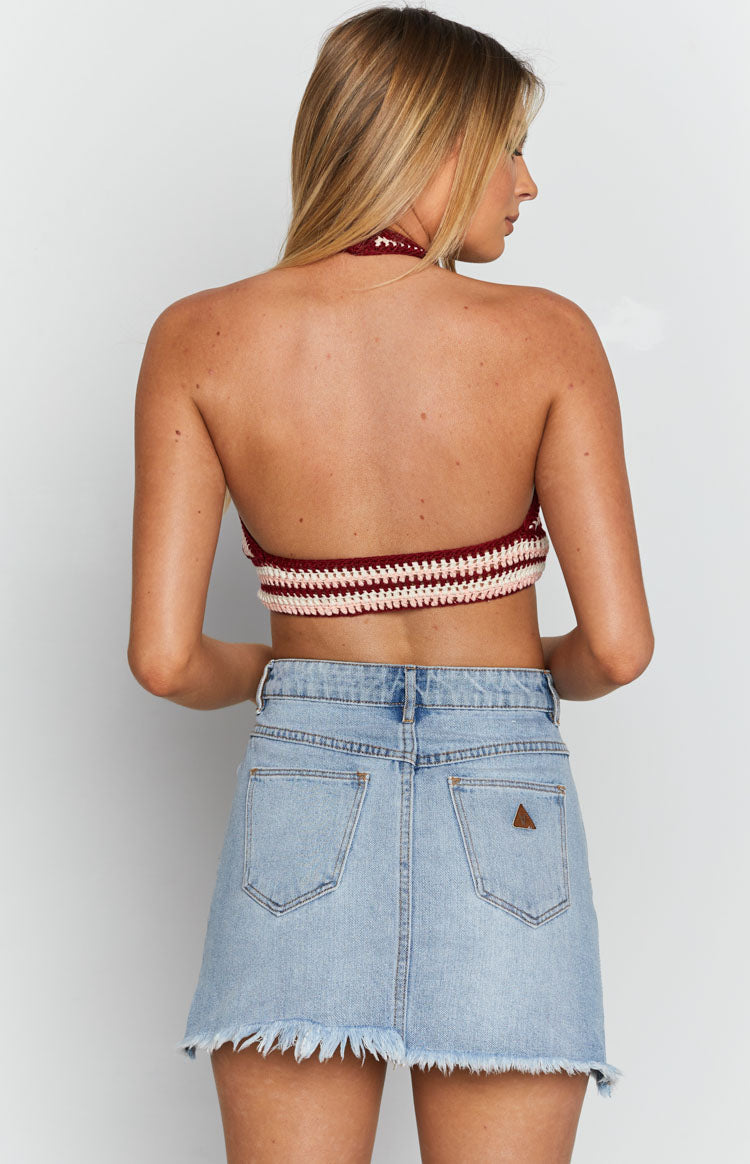 Light blue denim A-line mini skirt with raw frayed hem, back pockets, and brown triangle patch