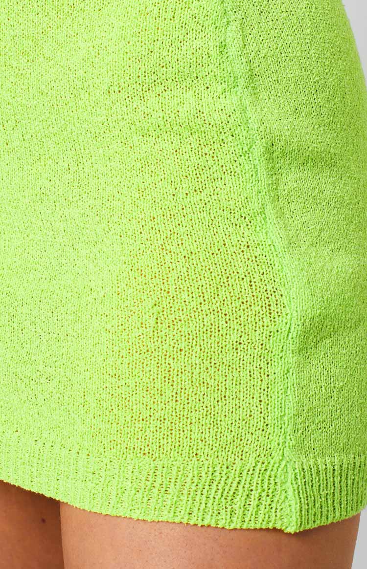 Close-up of the neon green open knit fabric and ribbed hem of a mini skirt