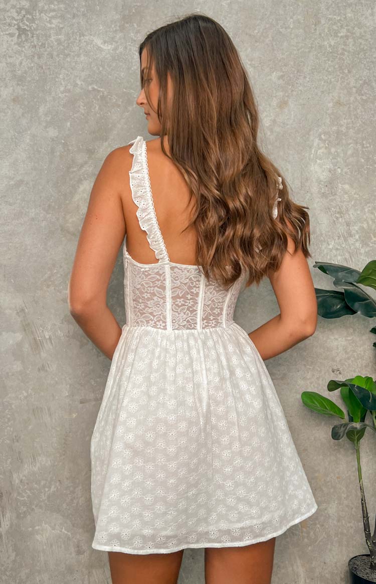 Side-rear view of a white mini dress showing the lace corset bodice, ruffled straps, and eyelet embroidered skirt