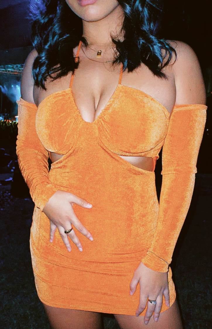 Close-up of the orange textured mini dress showing the deep V-neck, off-shoulder long sleeves, and waist cutouts
