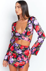 Detail shot of the black satin long sleeve wrap top with red, purple, and pink floral print, showing the deep V-neck and criss-cross waist cutouts
