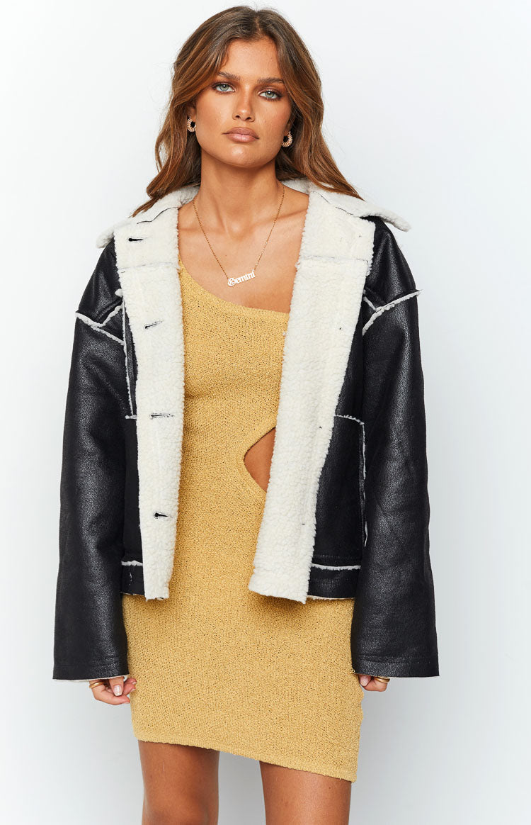 Front view of an open black faux leather jacket with cream faux fur lining and white stitching details