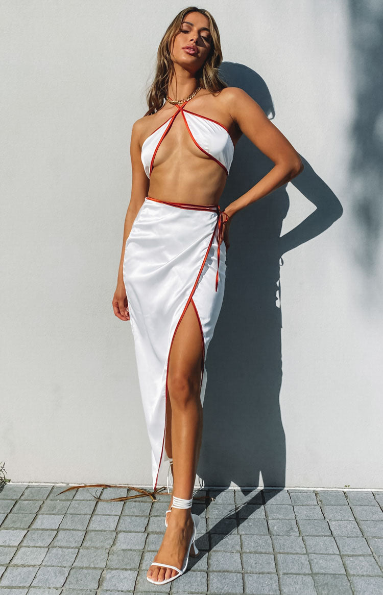 Front view of a white satin halter crop top with red trim, criss-cross straps, and open midriff